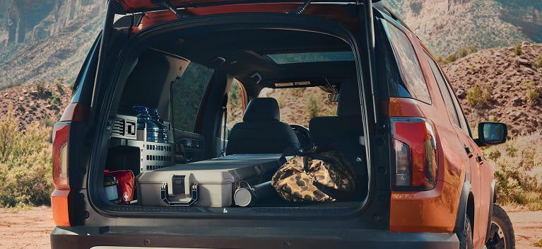 2026 Honda Passport TrailSport Elite in Sunset Orange back with open tailgate showing cargo in a desert (Mid-Size SUV).