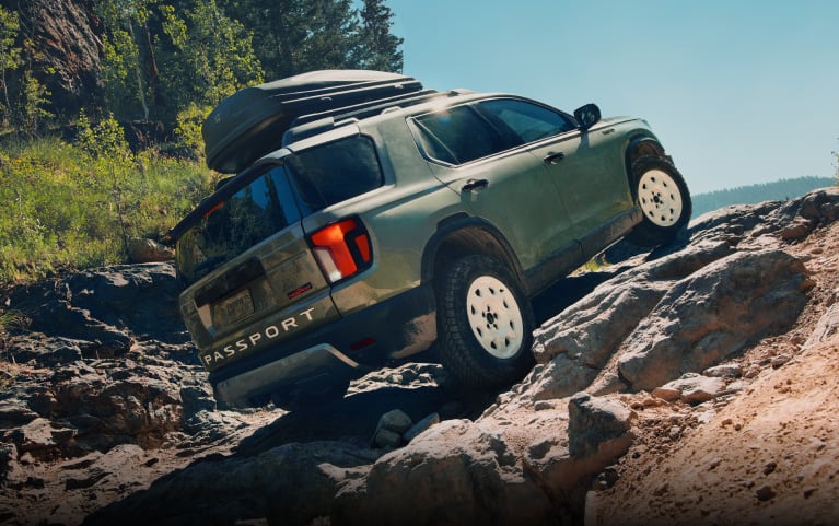 2026 Honda Passport TrailSport Elite in Ash Green Metallic back climbing a rocky off-road terrain (Mid-Size SUV).